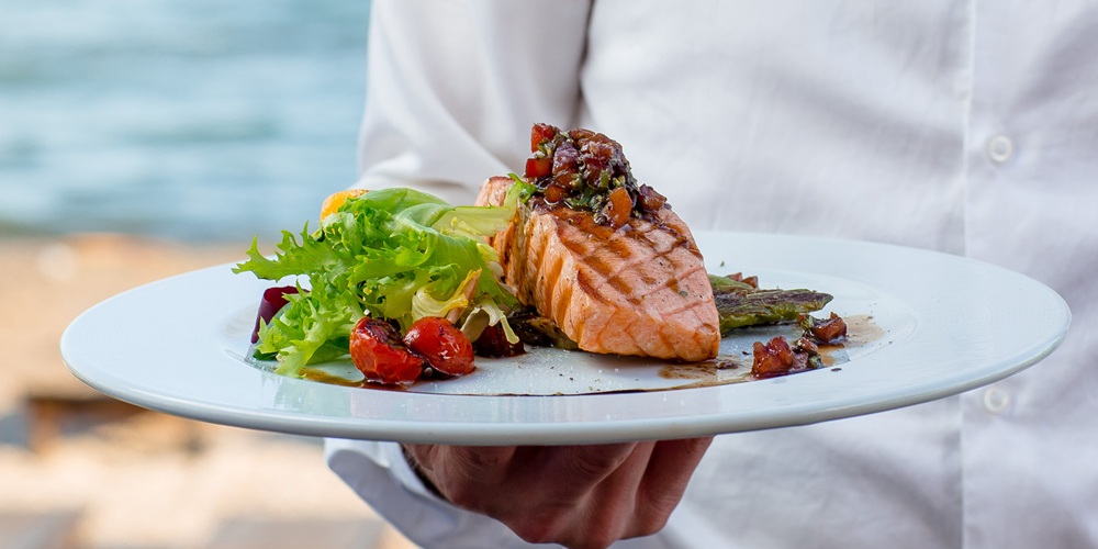 waiter holds a plate of grilled smoked salmon with lettuce, tomato, pepper waiter holds a plate of grilled smoked salmon with lettuce, tomato, pepper